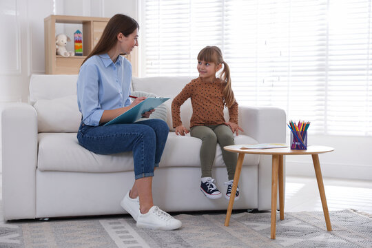 Professional psychologist working with little girl on sofa indoors