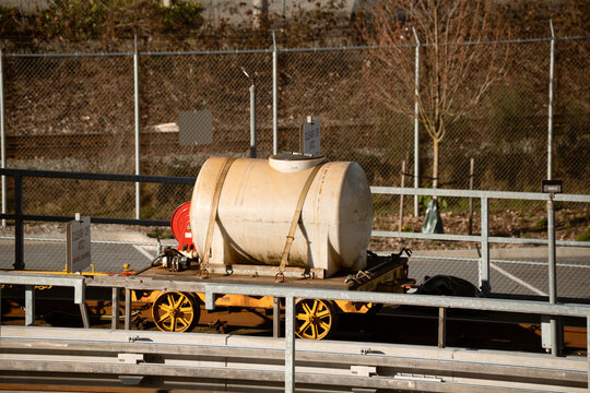 Industrial water tank on a railway flatcar with yellow wheels and safety straps