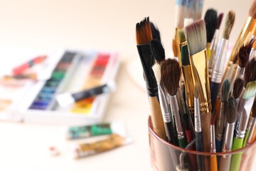 Obraz premium Paintbrushes in glass and paints on beige background, selective focus. Space for text