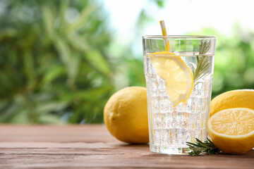 Fototapeta premium Lemon water with rosemary in glass and citrus fruits on wooden table against blurred background, closeup. Space for text