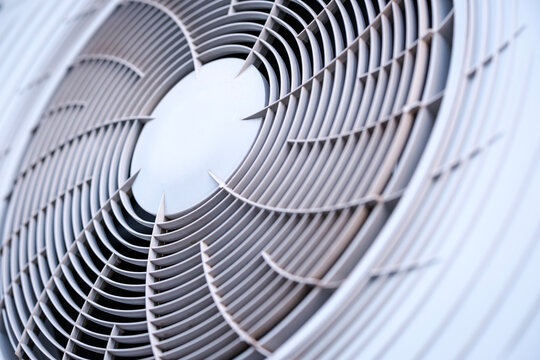 Fascinating abstract geometric pattern created by the circular gray plastic ventilation grille covering the rotating fan blades of a modern outdoor air conditioning unit