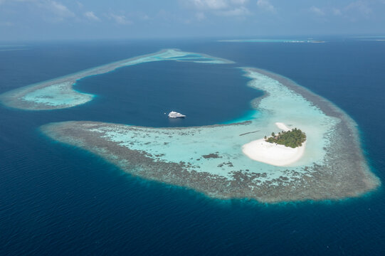 Wide aerial shot of luxury diving liveaboard yacht parked near Maldives atoll reef