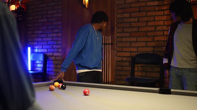 Young friends enjoying a night out playing a game of pool. An african american man breaks the rack of balls with a powerful shot
