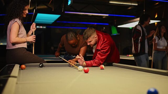 Man teaching a woman how to play pool while friends are watching, having fun together in a bar