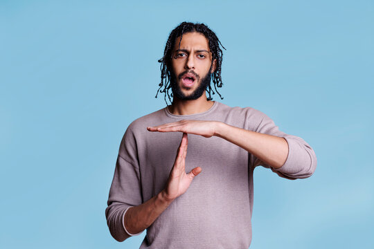 Arab man making time out gesture with hands and looking at camera portrait. Handsome young person showing interruption sign with arms, taking break from communication concept