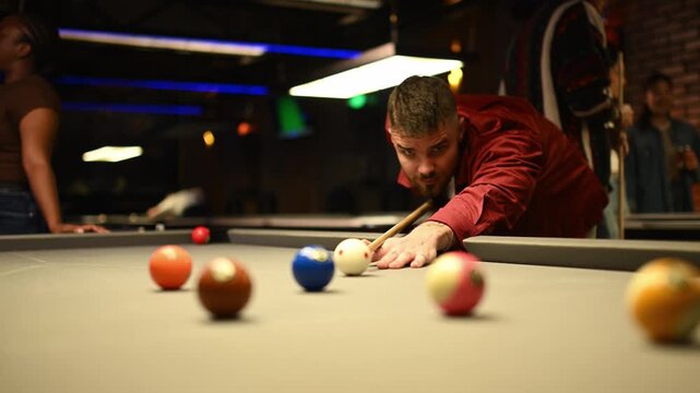Focused man aiming cue ball playing billiards game in a pool hall bar with friends at night