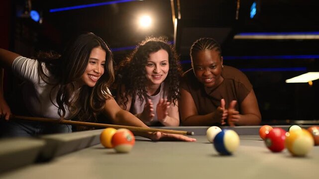 Three happy multi ethnic female friends playing pool together in a bar enjoying a game of billiards and having fun on a night out
