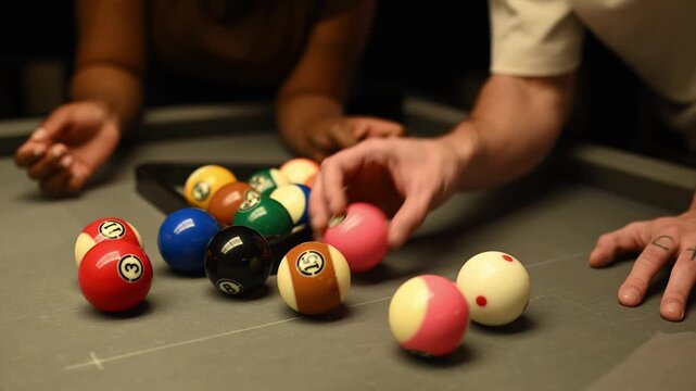 Close up of diverse couple racking billiard balls together preparing for a game of pool on a grey felt table at night