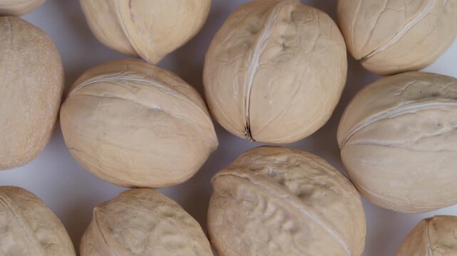 Arrangement of walnuts with shells. Display of striped walnut shells on warm beige surface. Closeup image featuring whole walnuts with textured shells on natural background