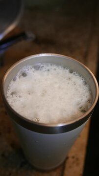 POV of someone filling a glass of beer on a table. Close-up of a person pouring beer into a glass. Close-up of bubbles bursting in a thick beer foam. Detail of a thick head of beer. A beer tumbler. 