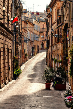 View of a narrow cobblestone alley lined with historic brick buildings and street lamps in Ripatransone, Marche, Italy.
