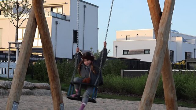 Litle girl swinging on a swing at a playground on a sunny day. Happy childhood moments, outdoor leisure activity, and active play in a natural environment. The child enjoys freedom, fun, and carefree 