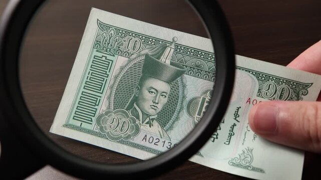 Examination of 10 Mongolian Tugrik cash money with magnfication glass, loupe. Concept of authenticity check, fight against counterfeiting of banknotes, anti fraud measures in Mongolia. Close up view.
