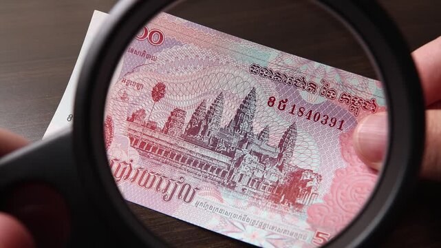 Examination of 500 Cambodian Riel (KHR) cash money with magnfication glass, loupe. Concept of authenticity check, fight against counterfeiting of banknotes, anti fraud measures in Cambodia.