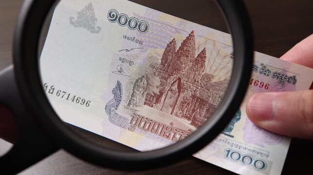Examination of 1000 Cambodian Riel (KHR) cash money with magnfication glass, loupe. Concept of authenticity check, fight against counterfeiting of banknotes, anti fraud measures in Cambodia.