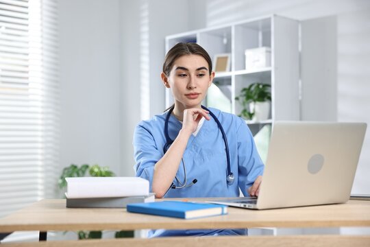 Young medical student studying with laptop at wooden table indoors