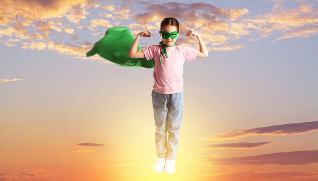 Little superhero. Girl in green mask and cape against sunset sky