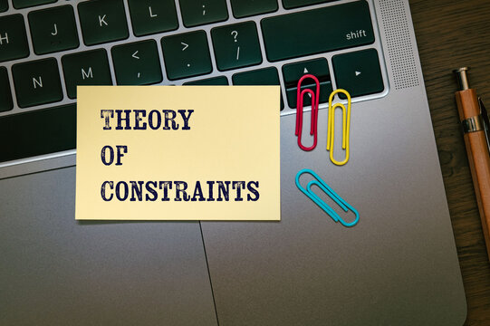 Corporate and management concept of Theory Of Constraints represented on sticky note with laptop, clips. Professional business leadership and operations.