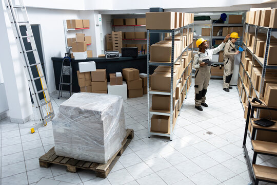 Black warehouse staff working in handling inventory for delivery, packaging cargo and dispatching goods. Industrial shelving units supports logistics and distribution process in depot.