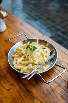 penne pasta are coated in a rich white sauce, tossed with pieces of savory bacon or pancetta, and generously topped with grated parmesan cheese and a fresh sprig of parsley