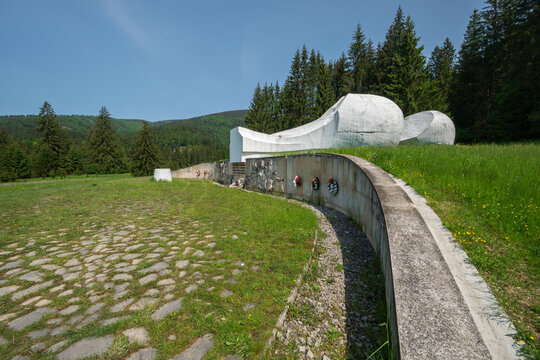 View of the Pamatnik SNP Vajskovska dolina monument featuring white concrete sculptures and a stone path set against pine forests in Dolna Lehota, Banskobystricky kraj, Slovakia.