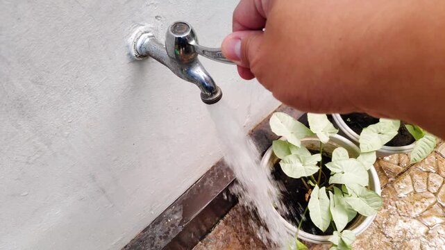 Man hand turning a chrome water tap in slow motion to start a flow in a home garden