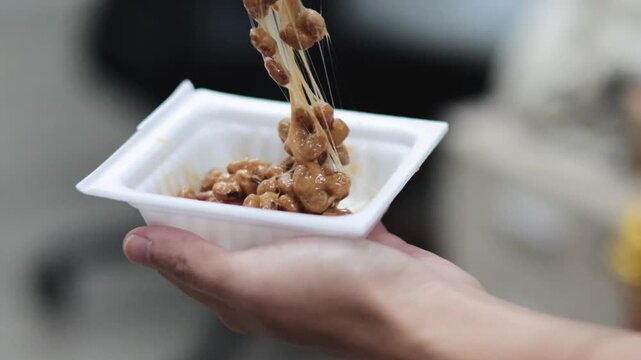 Close up of natto fermented soybeans being stirred with chopsticks revealing sticky threads motion.