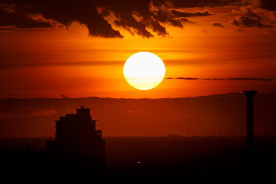 A large sun sets behind clouds in a dramatic red sunset sky