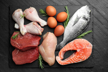 Naklejka premium Different types of fresh raw meat, fish, eggs and rosemary on black table, top view