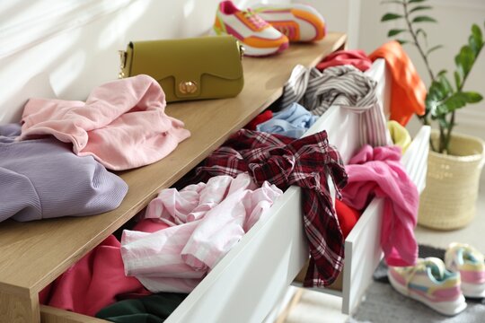 Chest of drawers with different messy clothes in room, closeup
