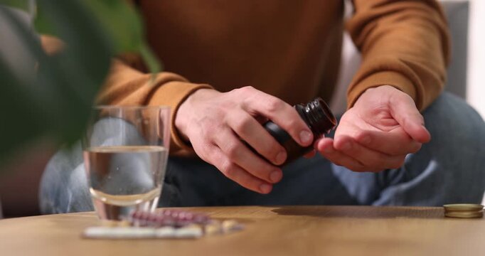 Man pouring pills from bottle at wooden table indoors, closeup