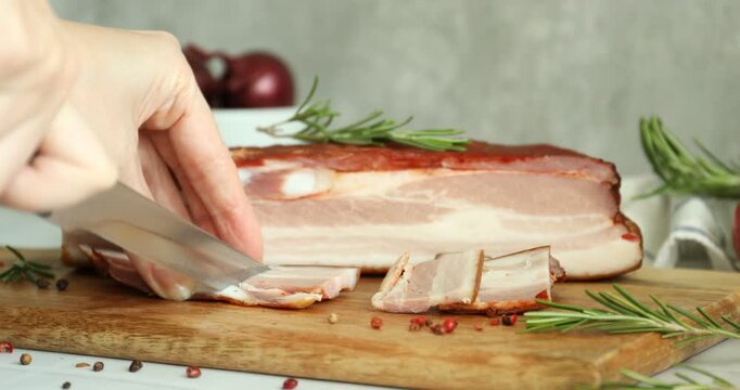 Woman cutting smoked bacon at light table against grey background, closeup