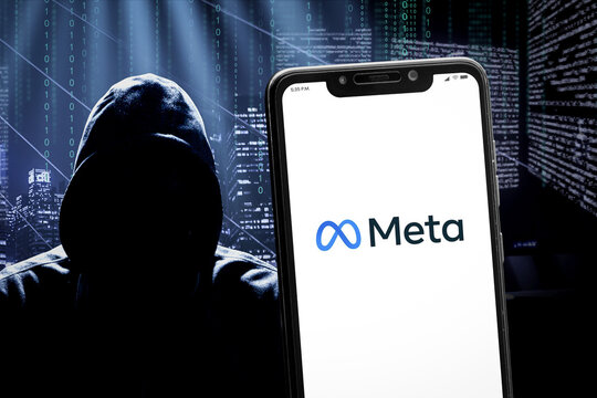 Cali, Colombia - April 20 2022: Smartphone displaying Meta logo against a blurred background with a hooded hacker silhouette and a dark cityscape with digital code.