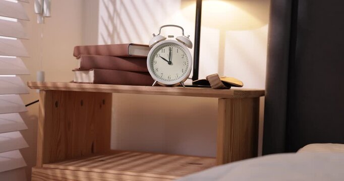 Woman putting sleeping mask next to alarm clock on bedside table indoors, closeup