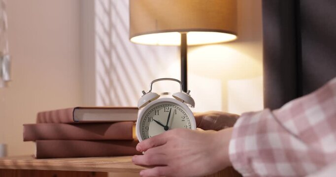 Woman stopping alarm clock at bedside table indoors, closeup