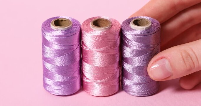 Woman putting spool of thread on pink background, closeup