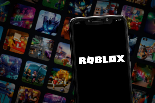 Cali, Colombia - May 6 2022: Smartphone displaying Roblox logo against blurred game thumbnails background.