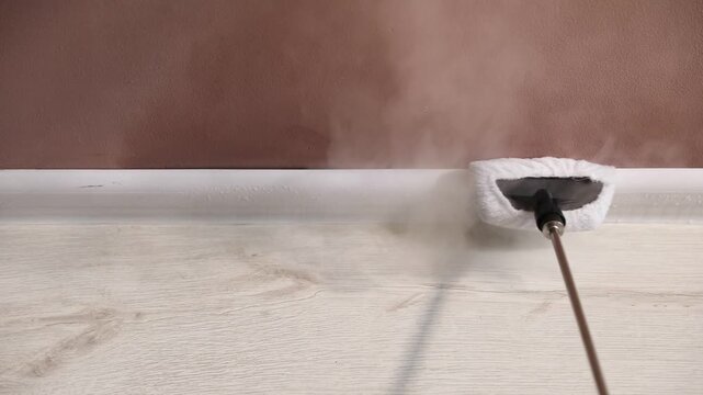Cleaning baseboard with steam cleaner near brown wall indoors, closeup