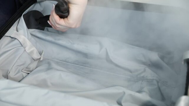 Woman cleaning open suitcase with steam cleaner on floor at home, closeup. Camera moving left