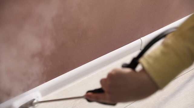 Woman cleaning baseboard with steam cleaner near brown wall indoors, above view
