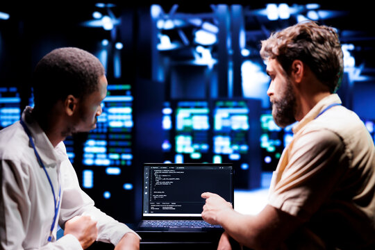 IT developers coworkers writing script code in server room on laptop terminal. Teamworking programmers doing maintenance work in technologically advanced data center updating racks software