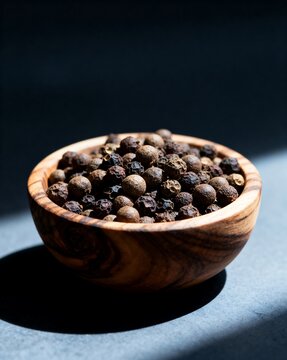 Wooden bowl filled with assorted peppercorns and spices, high contrast lighting