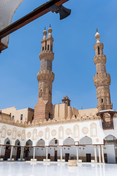View of the Al-Azhar Mosque featuring ornate stone minarets and a white marble courtyard under a clear blue sky in Cairo, Egypt.