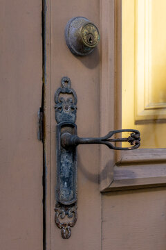 A cream colored wooden door with a half-glass window. There's a brass deadbolt lock and an ornate, long-handle winding knob for an exterior door. The handle is made of cast iron metal in a key shape.