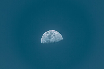 Sharp third quarter moon with detailed craters against a deep teal sky with copy space © Jaziel