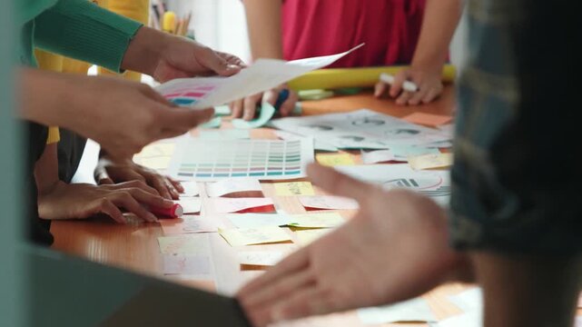 Top view of business team write graphic logo on meeting table with colorful sticky notes and design while explain idea. Project manager sharing idea and explain concept art to smart team. Symposium.