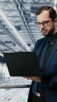Vertical video Portrait of cheerful man looking at data on laptop, improving microchips fabrication supply chain yield. Jolly manager visualizing semiconductors factory production line bottlenecks