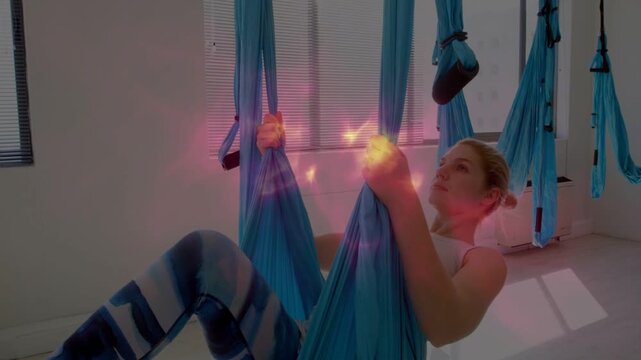 Woman gripping blue hammock straps, pulling back into reclined pose for back stretch