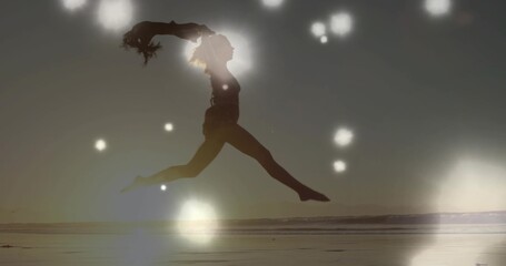 Fototapeta premium Leaping mid adult female wearing leotard doing split leap across wet sand beach with lens flares
