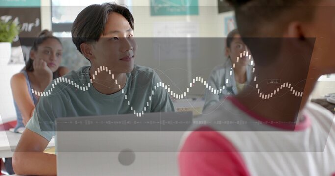 Watching teen Asian male student focusing in classroom, using laptop with waveform HUD